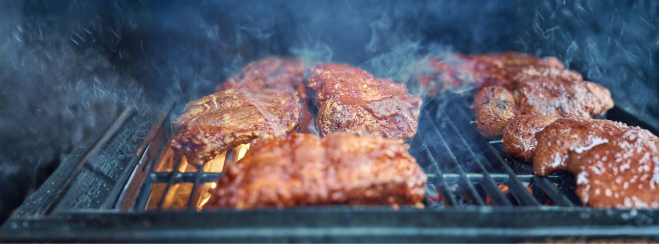 A rack of ribs smoking on a barbecue with visible smoke rising