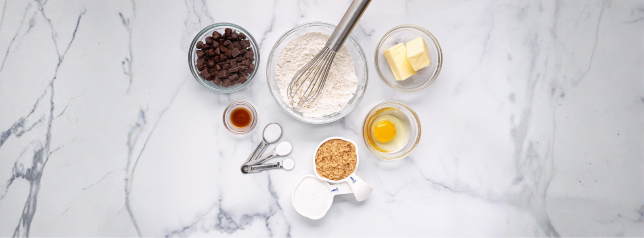 Baking ingredients laid out on a counter — flour, eggs, butter, sugar, measuring cups