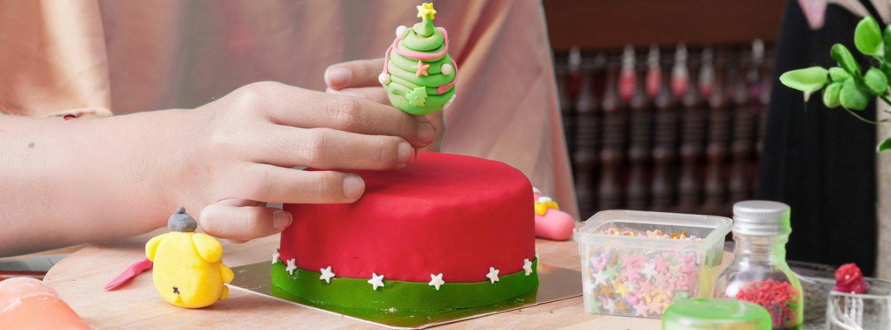 Hands sculpting a small fondant figure on a cake-decorating board