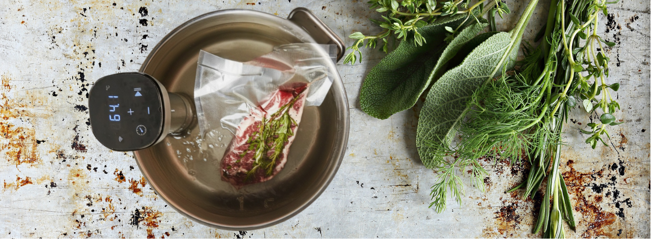 Vacuum-sealed steak with herbs and butter cooking in a sous vide water bath.