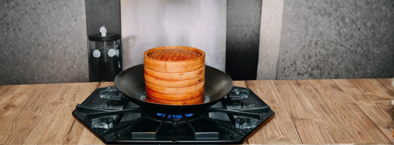 Vegetables steaming in a bamboo steamer over a pot of water