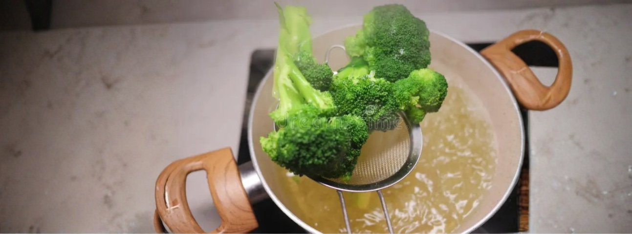 bright green vegetables being lifted from boiling water with a slotted spoon